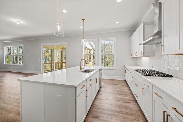 kitchen with wall chimney range hood, crown molding, backsplash, and a sink