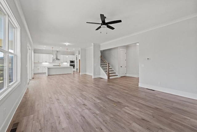 unfurnished living room featuring plenty of natural light, stairway, light wood-style flooring, and ornamental molding