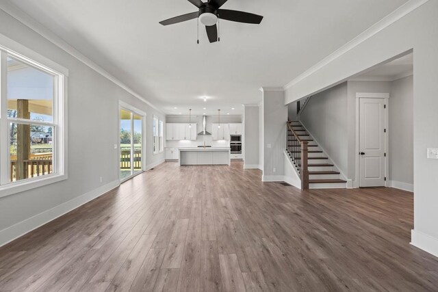 unfurnished living room with a ceiling fan, baseboards, stairs, light wood-style floors, and ornamental molding