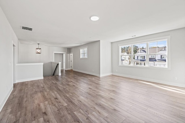 unfurnished living room featuring a notable chandelier, wood finished floors, visible vents, and baseboards