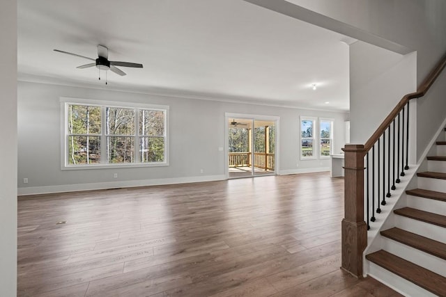 unfurnished living room with stairs, ceiling fan, baseboards, and wood finished floors