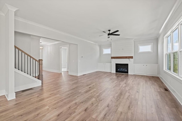 unfurnished living room with a ceiling fan, a glass covered fireplace, light wood-style flooring, stairway, and ornamental molding