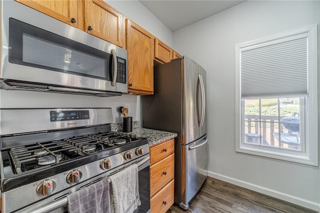 2164 Mill Garden Run, Buford, GA 30519 - kitchen featuring brown cabinetry, stone countertops, appliances with stainless steel finishes, dark wood-style flooring, and baseboards