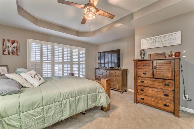 bedroom with light colored carpet, baseboards, a tray ceiling, and ceiling fan