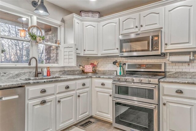 kitchen with light stone countertops, a sink, decorative backsplash, stainless steel appliances, and white cabinets