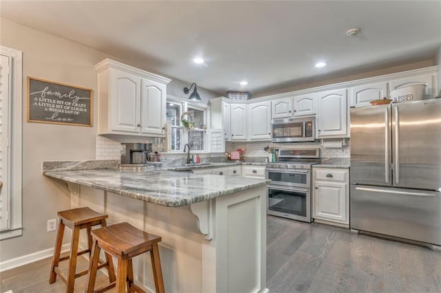 kitchen featuring dark wood-type flooring, white cabinetry, a peninsula, appliances with stainless steel finishes, and a breakfast bar area