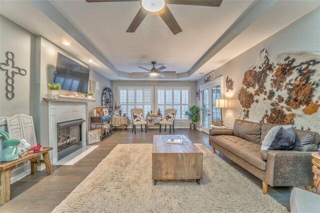 living area featuring a raised ceiling, a fireplace, dark wood-type flooring, and ceiling fan