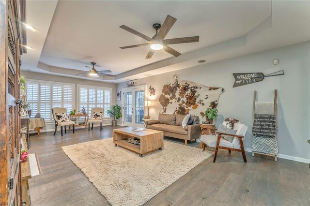 living room featuring a raised ceiling, wood finished floors, baseboards, and french doors