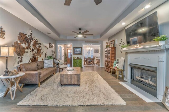 living area featuring wood finished floors, baseboards, a fireplace, ceiling fan, and a raised ceiling