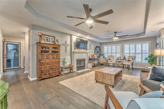 living room with dark wood-style floors, ceiling fan, a fireplace, and a tray ceiling