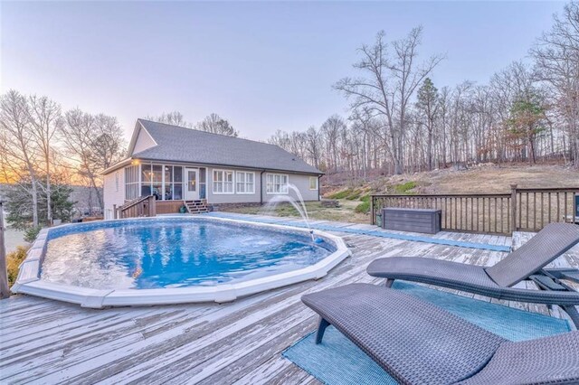 pool at dusk with a fenced in pool, a sunroom, and a wooden deck