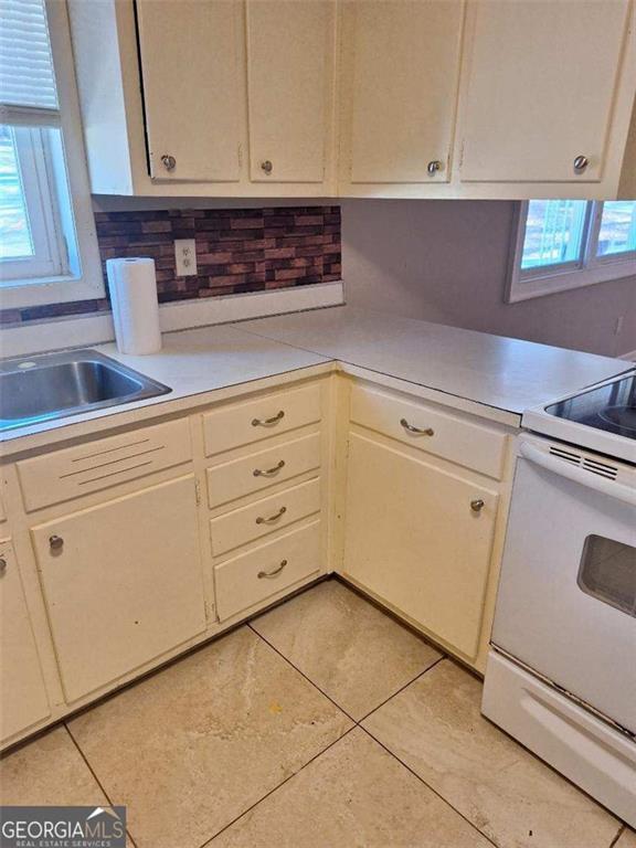 kitchen with electric stove, light countertops, a sink, and light tile patterned floors