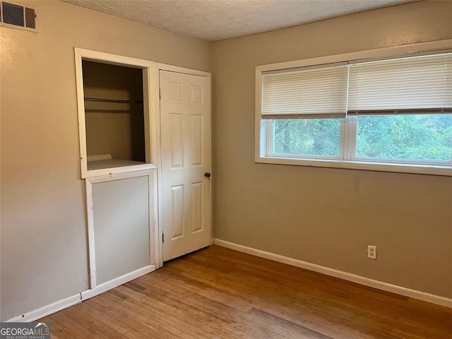 unfurnished bedroom featuring a closet, visible vents, a textured ceiling, wood finished floors, and baseboards