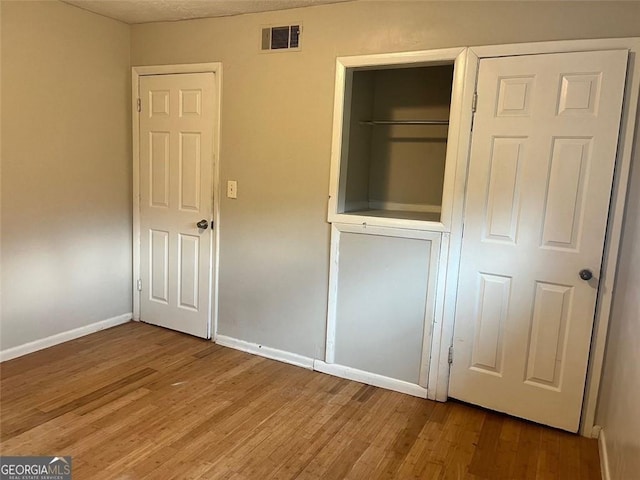 unfurnished bedroom featuring a closet, wood finished floors, visible vents, and baseboards