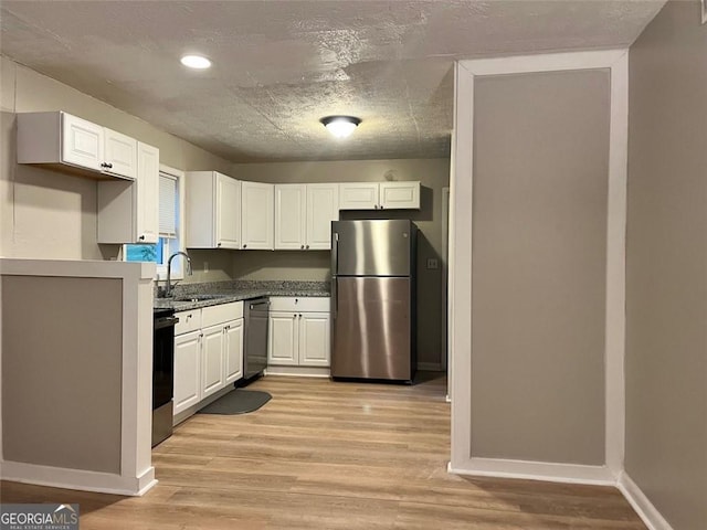 kitchen with stove, light wood-style floors, freestanding refrigerator, white cabinets, and a sink