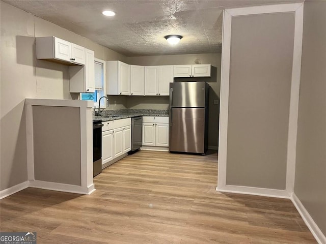 kitchen featuring light wood-style flooring, a sink, white cabinets, baseboards, and freestanding refrigerator