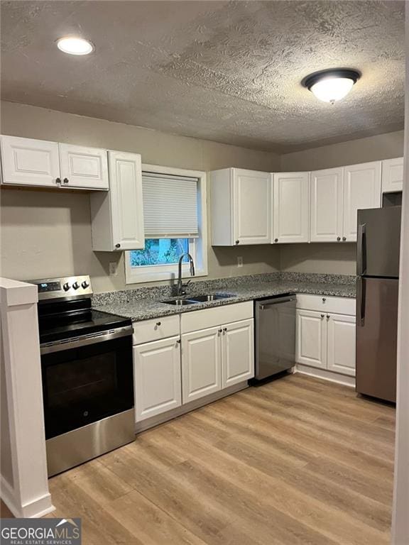 kitchen with appliances with stainless steel finishes, white cabinetry, a sink, and light wood finished floors