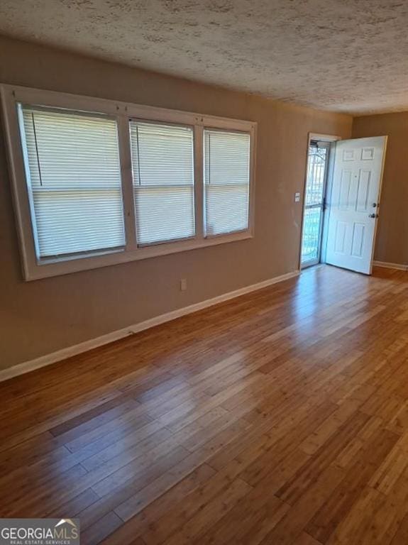 unfurnished room featuring hardwood / wood-style flooring, baseboards, and a textured ceiling