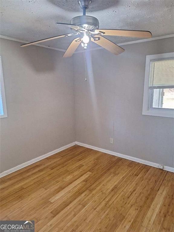 empty room featuring a textured ceiling, light wood-style flooring, a ceiling fan, baseboards, and ornamental molding