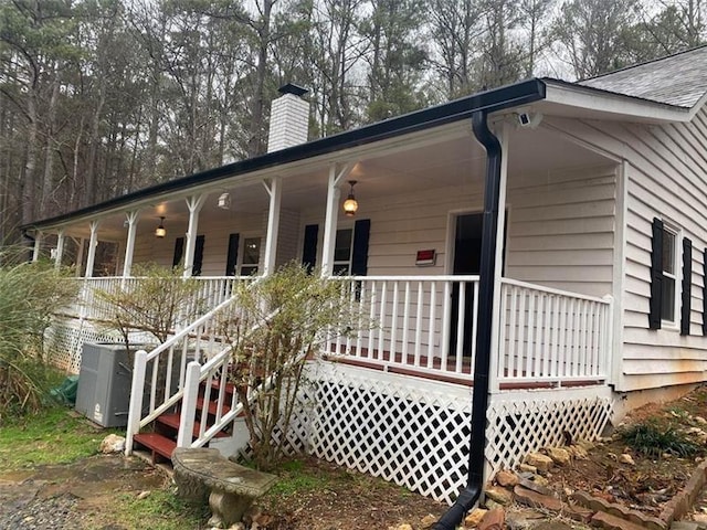 back of house featuring cooling unit, a porch, and a chimney