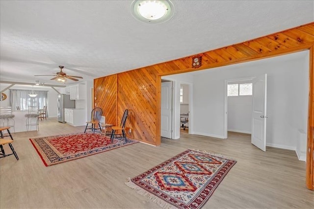 living area featuring wooden walls, a textured ceiling, baseboards, and wood finished floors