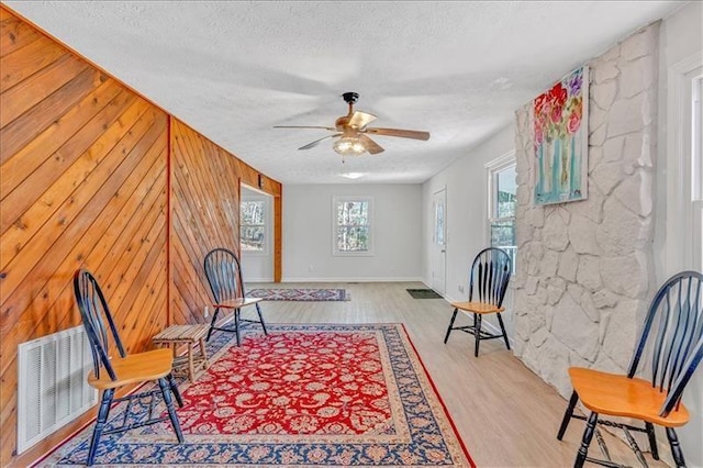 living area with visible vents, a textured ceiling, wood finished floors, wooden walls, and ceiling fan