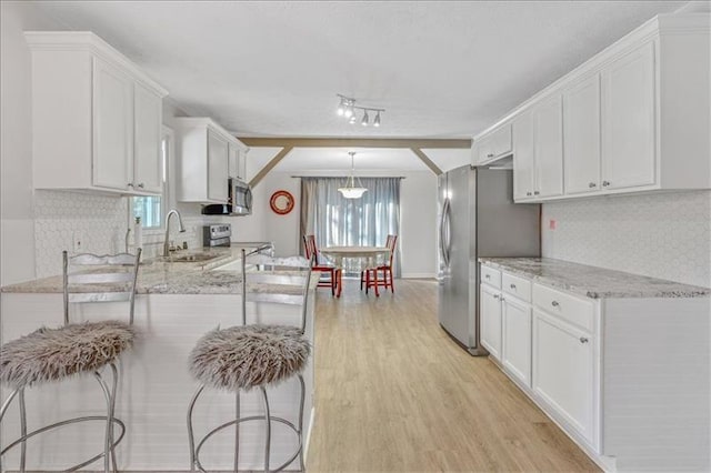 kitchen with plenty of natural light, stainless steel appliances, white cabinets, light wood finished floors, and light stone countertops