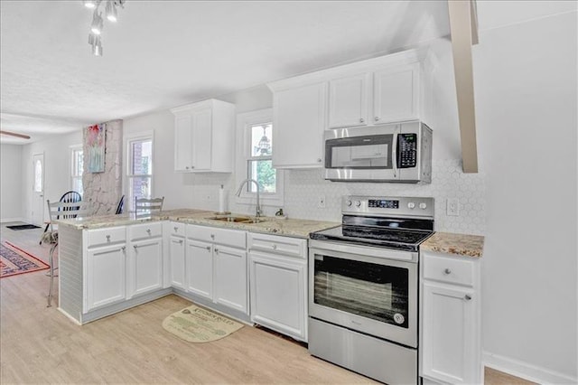 kitchen with tasteful backsplash, appliances with stainless steel finishes, a peninsula, white cabinetry, and a sink