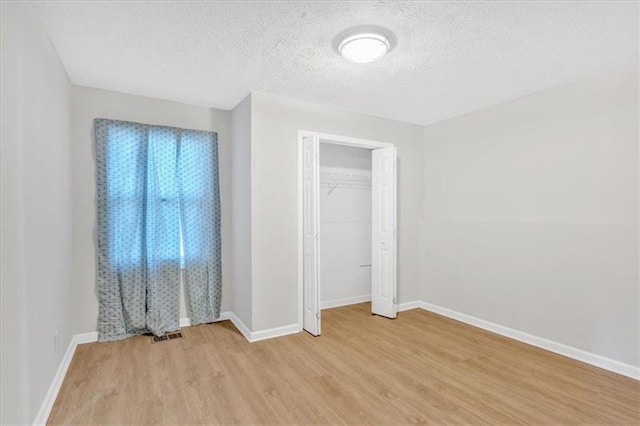 unfurnished bedroom featuring light wood-style floors, baseboards, a closet, and a textured ceiling