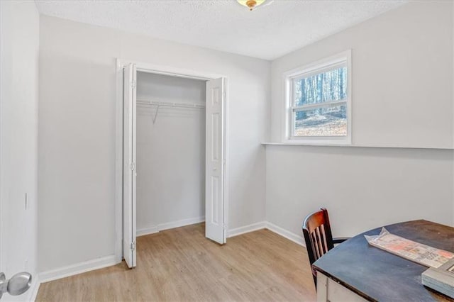 interior space featuring baseboards, a textured ceiling, and light wood finished floors