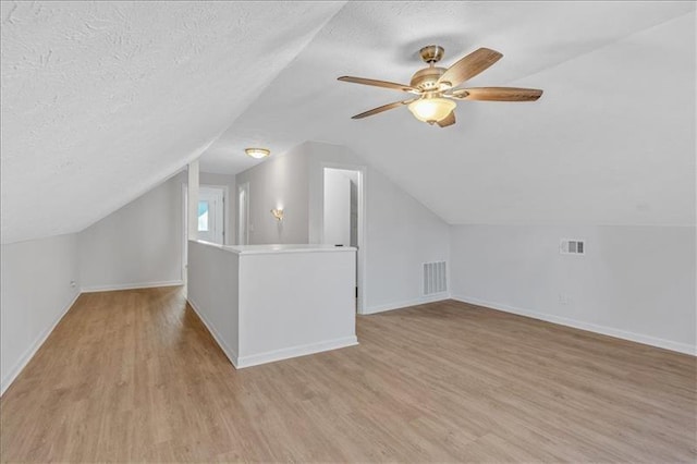 bonus room with light wood-style floors, visible vents, baseboards, and a textured ceiling