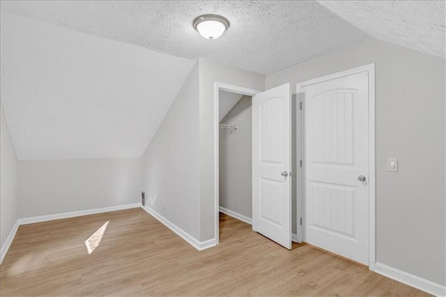 additional living space featuring lofted ceiling, light wood-style floors, baseboards, and a textured ceiling