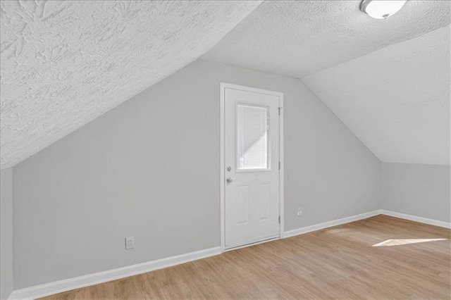 bonus room featuring lofted ceiling, a textured ceiling, light wood-type flooring, and baseboards