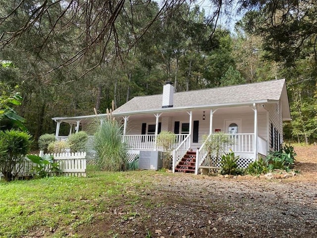 ranch-style home featuring central AC unit, covered porch, a chimney, and a shingled roof