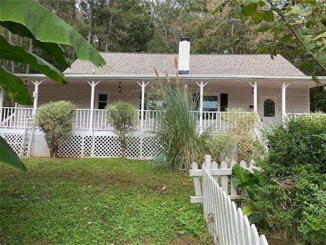 back of house with a yard, a porch, a chimney, and a shingled roof