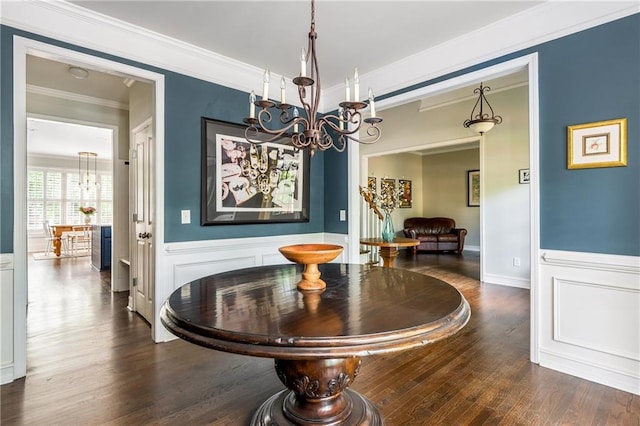 dining room featuring a chandelier, dark wood-style floors, crown molding, wainscoting, and a decorative wall