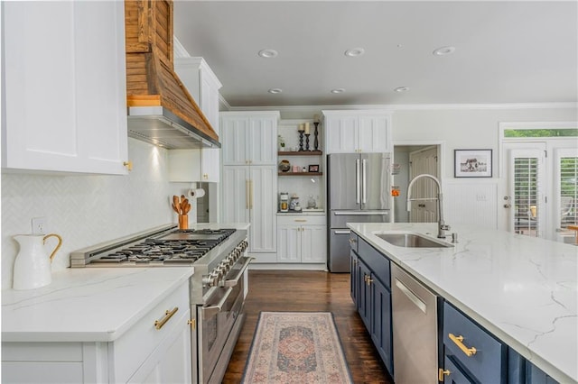 kitchen with appliances with stainless steel finishes, a sink, blue cabinetry, custom exhaust hood, and white cabinetry