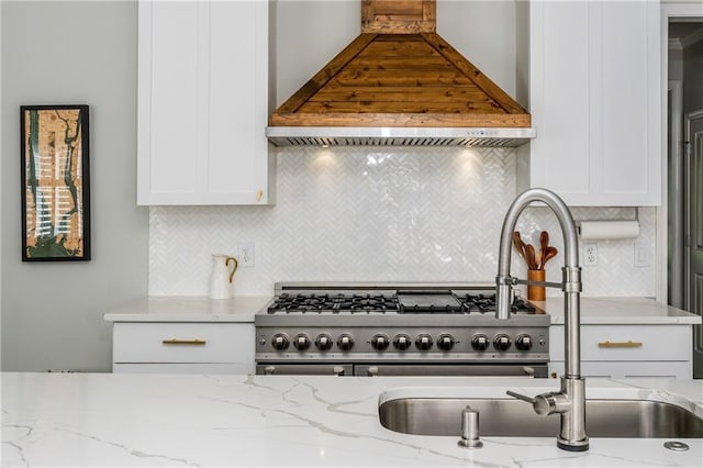 kitchen featuring wall chimney range hood, white cabinetry, backsplash, and light stone counters