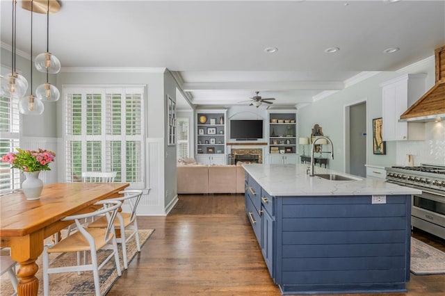 kitchen with a sink, ceiling fan, blue cabinets, a warm lit fireplace, and dark wood-style floors
