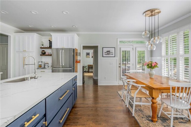 kitchen with a sink, freestanding refrigerator, blue cabinets, white cabinets, and crown molding
