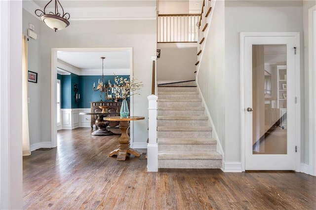 staircase featuring wood finished floors, ornamental molding, baseboards, and a chandelier