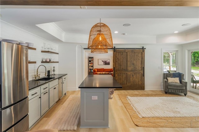 kitchen featuring a raised ceiling, stainless steel appliances, a sink, dark countertops, and crown molding