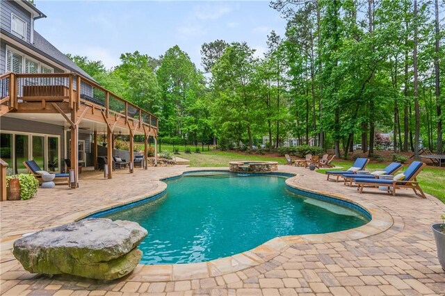 view of swimming pool featuring a patio area, a deck, a pool with connected hot tub, and view of scattered trees