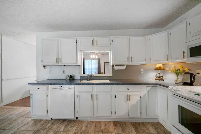 kitchen featuring white appliances, white cabinets, a sink, dark countertops, and a textured ceiling