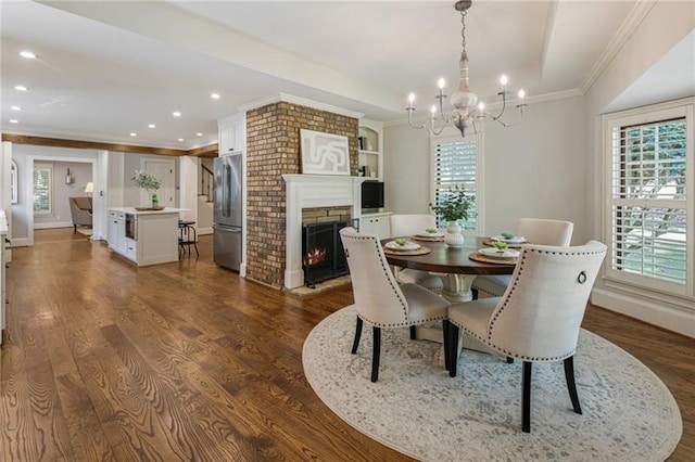 dining space featuring dark wood-type flooring, a chandelier, a healthy amount of sunlight, and a fireplace