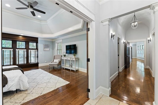 bedroom featuring a raised ceiling, dark hardwood / wood-style flooring, ceiling fan with notable chandelier, and crown molding