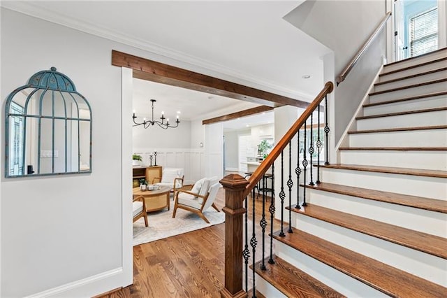 stairway with a chandelier, ornamental molding, and wood-type flooring