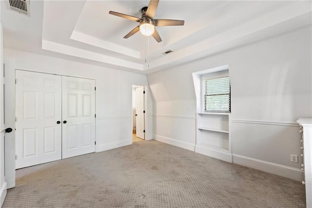 unfurnished bedroom featuring ceiling fan, light carpet, a closet, and a tray ceiling