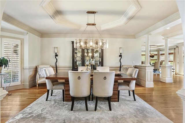 dining area featuring a raised ceiling, wood finished floors, crown molding, and decorative columns