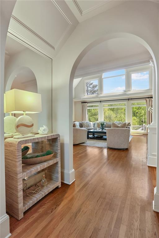hallway featuring lofted ceiling, wood finished floors, arched walkways, and a healthy amount of sunlight